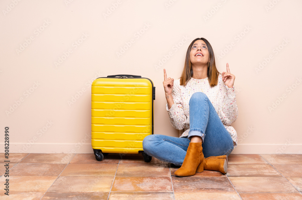 Traveler woman with suitcase sitting on the floor pointing with the index finger a great idea Traveler woman with suitcase sitting on the floor pointing with the index finger a great idea