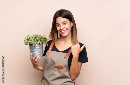Young woman holding a plant pointing to the side to present a product