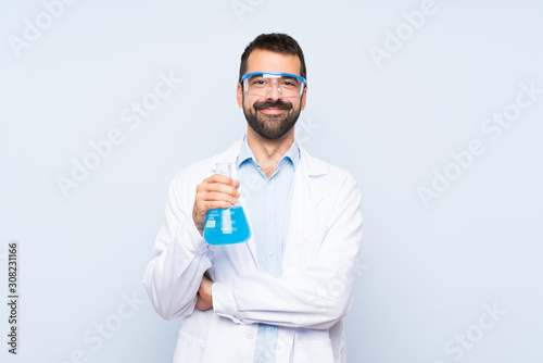 Young scientific holding laboratory flask over isolated background keeping the arms crossed in frontal position