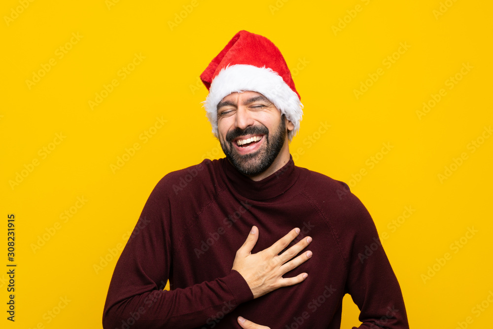 Man with christmas hat over isolated yellow background smiling a lot