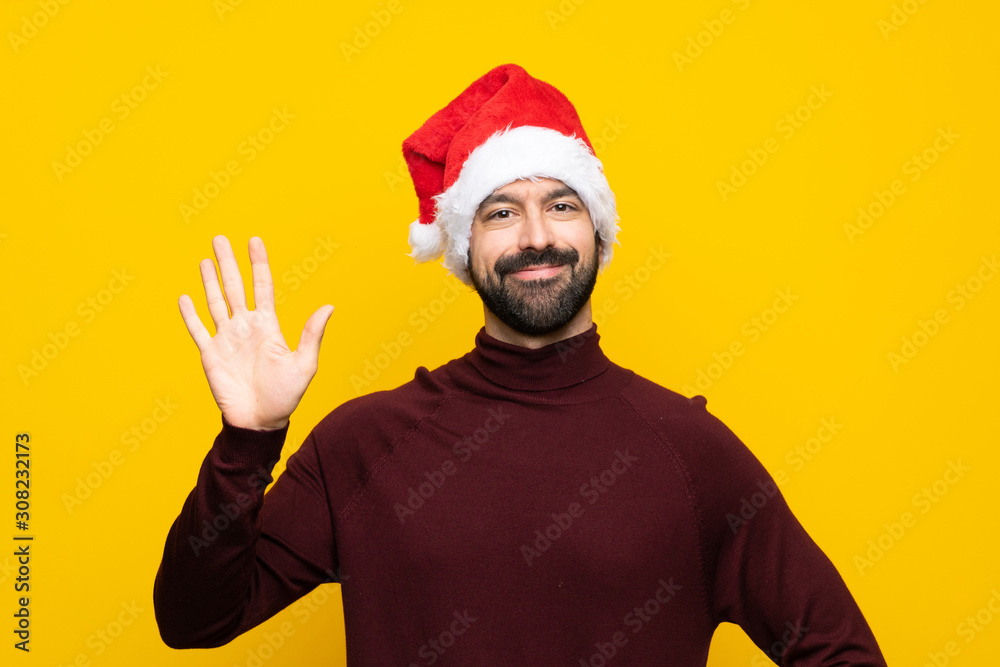 Man with christmas hat over isolated yellow background saluting with hand with happy expression Man with christmas hat over isolated yellow background saluting with hand with happy expression