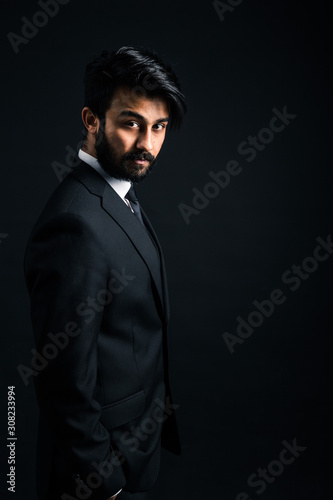 Portrait of a young handsome successful Indian in a classic black three-piece business suit on a dark background