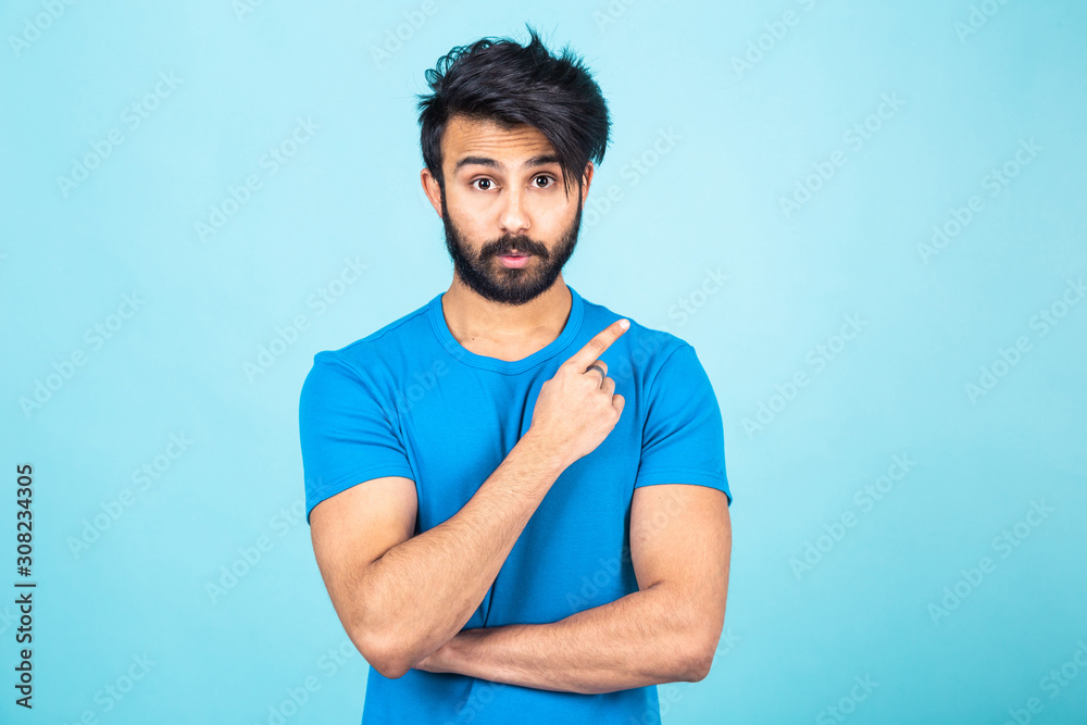 Emotional portrait of a handsome Hindu man in a blue T-shirt on a bright blue background, points finger to empty space Emotional portrait of a handsome Hindu man in a blue T-shirt on a bright blue background, points finger to empty space
