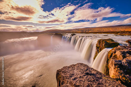 Goðafoss in long exposer, blue sky, warm autumn colors in the Sun rays
