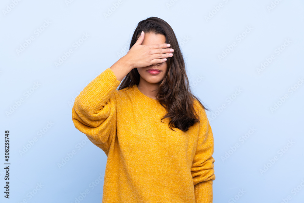 Young Colombian girl with sweater over isolated blue background covering eyes by hands. Do not want to see something Young Colombian girl with sweater over isolated blue background covering eyes by hands. Do not want to see something