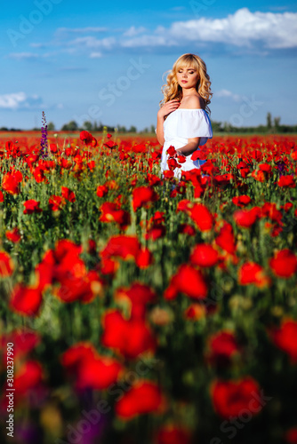 cheerful girl with curly blond hair in a huge poppy field alone, springtime, sunset