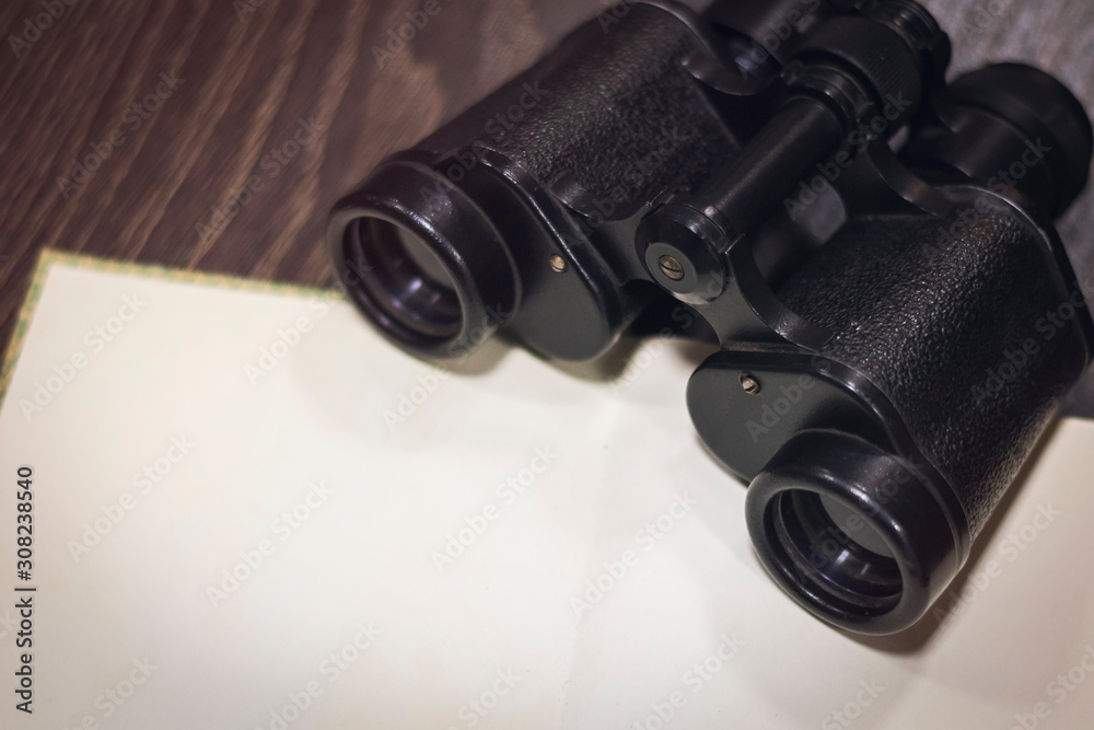 vintage binoculars on a dark wooden background with an open book with blank blank pages