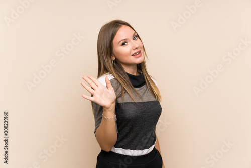 Teenager girl over isolated background saluting with hand with happy expression