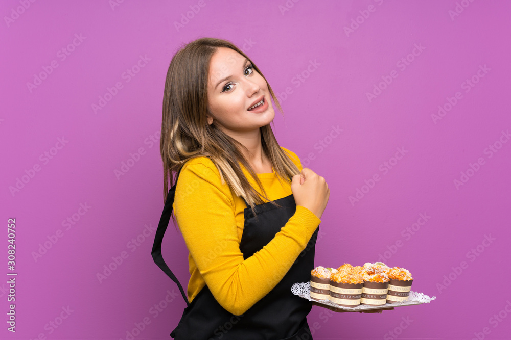 Teenager girl holding lots of different mini cakes over isolated purple background celebrating a victory Teenager girl holding lots of different mini cakes over isolated purple background celebrating a victory