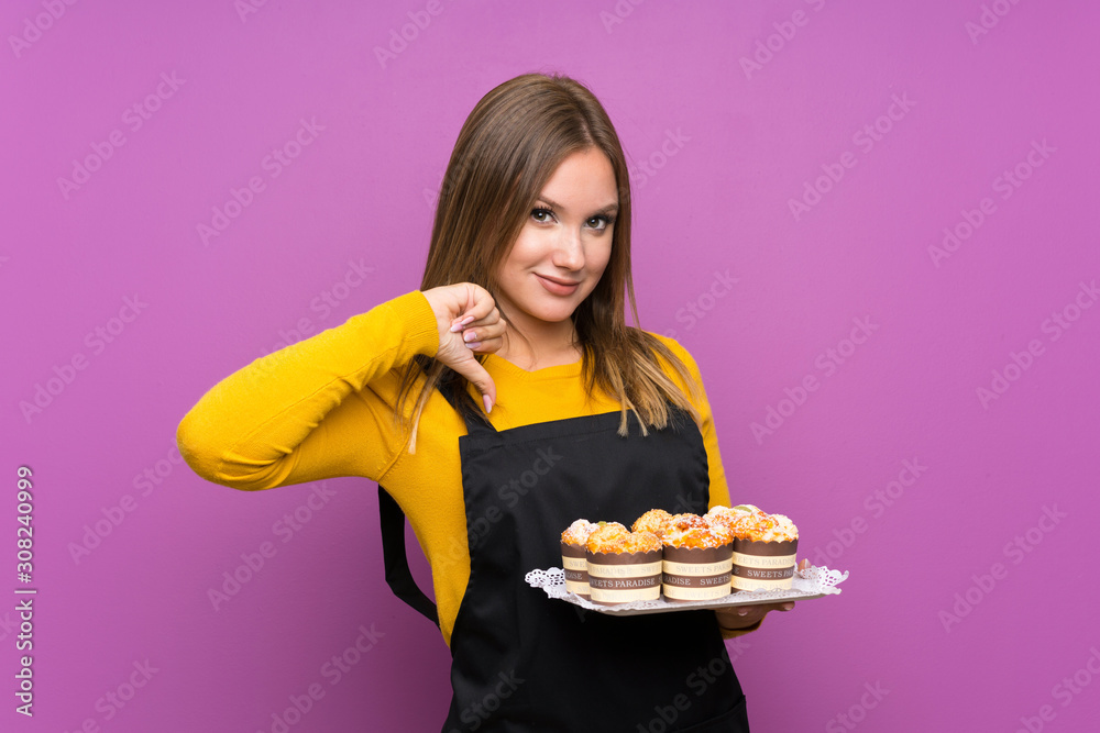 Teenager girl holding lots of different mini cakes over isolated purple background proud and self-satisfied Teenager girl holding lots of different mini cakes over isolated purple background proud and self-satisfied