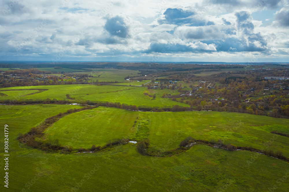 Obraz premium Green fields and rivers under a picturesque sky with clouds. Autumn landscape from above view