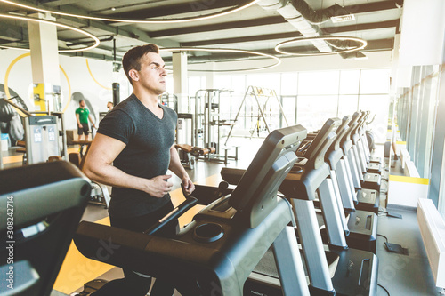 The athletic man dressed in a black sportswear running on the treadmill in the modern gym