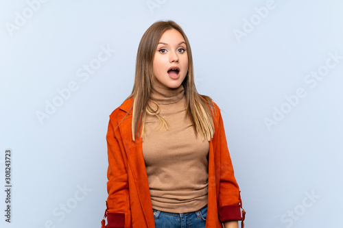 Teenager girl with coat over isolated blue background with surprise facial expression