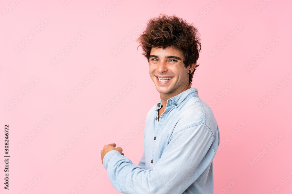 Young caucasian man with jean shirt over isolated pink background pointing back Young caucasian man with jean shirt over isolated pink background pointing back