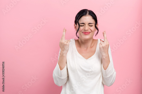 Young woman crossing her fingers and wishing for good luck on a pink background