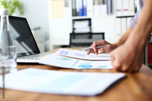 Male hands on the office desk. Young businessman holding a pen in hand and studies the results of sales represented on the graphics. Concept of office workplace.