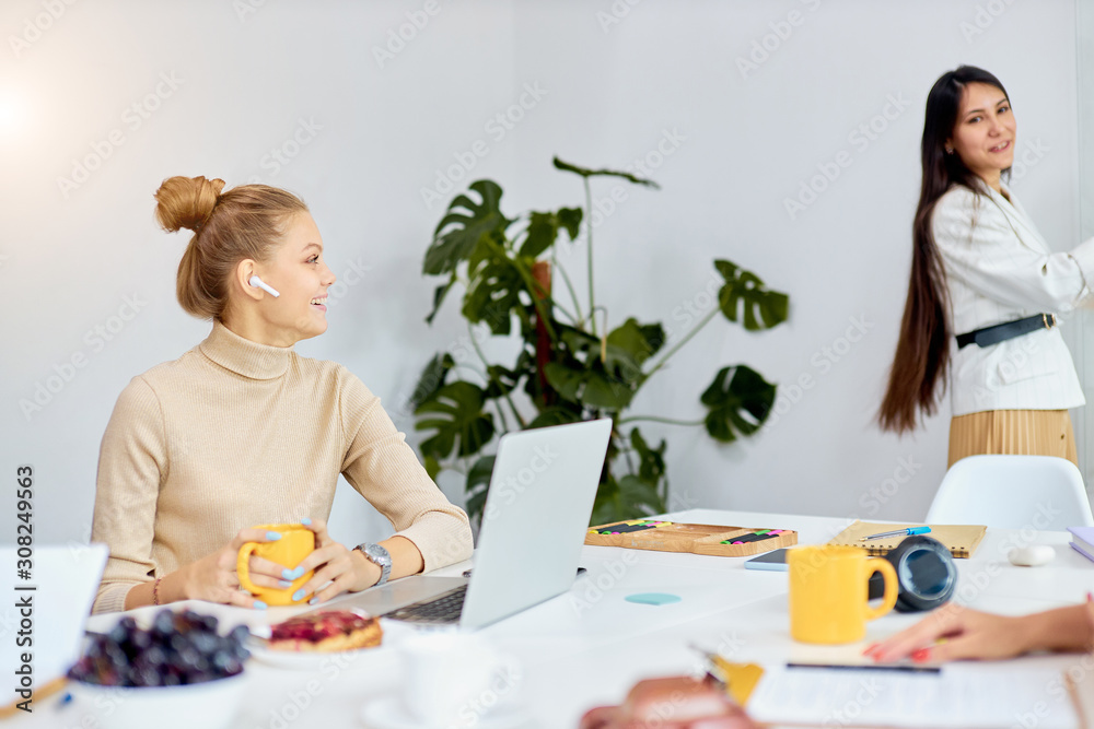 side view on modern young caucasian woman with headphones sit looking at speaker and laugh in office, use laptop