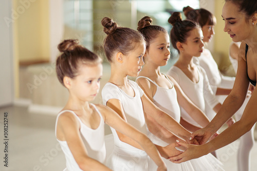 attractive and beautiful caucasian woman wearing black tutu skirt show right poses in ballet to little kids, performing ballet dance in studio, isolated in ballet school