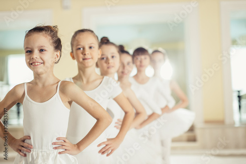 little caucasian girls in white tutu skirts and pointe shoes dream of becoming great ballerinas, training, practicing classic ballet dance in studio, group of little caucasian graceful girls