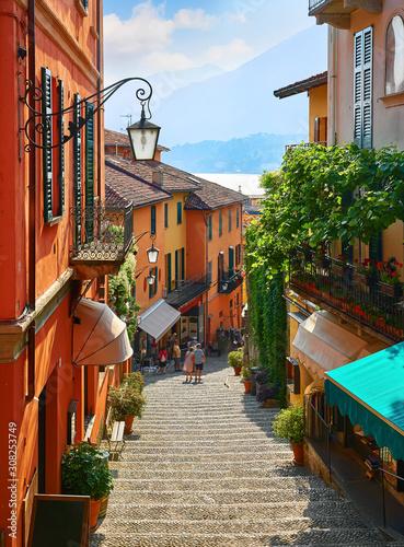 Bellagio village at lake Como near Milan Italy, region Lombardy. Famous street with paving stones stairs and cosy restaurants during sunrise with glowing lanterns and green plants on old houses walls.