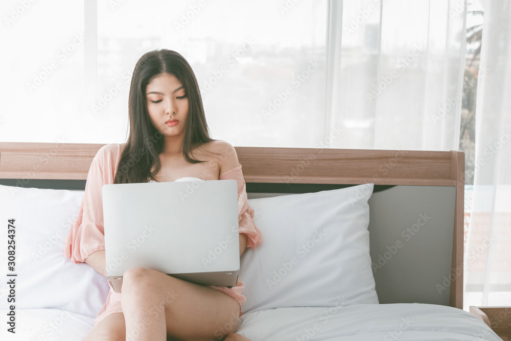 Beautiful woman using notebook computer on the bed in bedroom on the morning background textures. Beautiful woman using notebook computer on the bed in bedroom on the morning background textures.