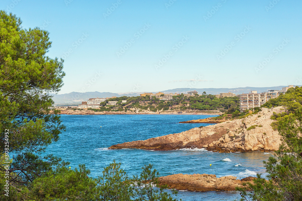 Seascape: blue sea with rocky shores and green trees. Spain, Costa Dorada, Salou