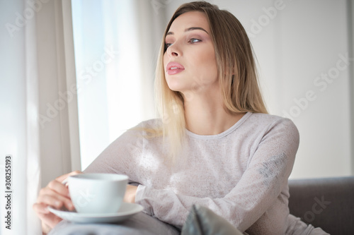 Enjoying morning coffee. Close-up of beautiful young woman holding cup while relaxing on couch at home