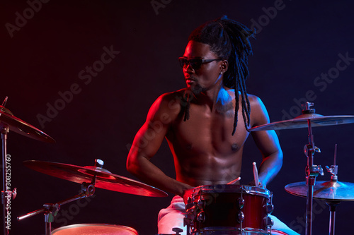 Fototapeta good-looking artistic african black male drummer enjoying playing drums over dar