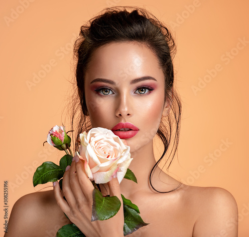 Beautiful white girl with rose.  Stunning brunette girl with white flower. Closeup face of young beautiful woman with a healthy clean skin. Pretty woman with bright makeup #308255916