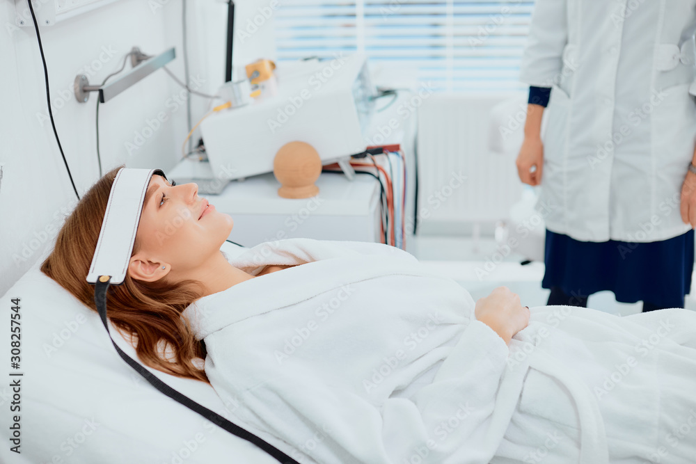 calm patient lying on bed and looking up with medical frontlet, wearing white bathrobe calm patient lying on bed and looking up with medical frontlet, wearing white bathrobe