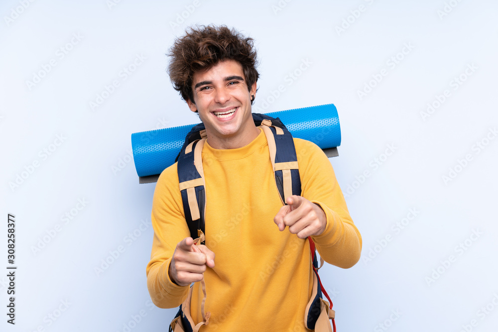 Young mountaineer man with a big backpack over isolated blue background points finger at you Young mountaineer man with a big backpack over isolated blue background points finger at you