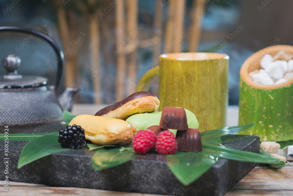 Sweet dessert, eclairs, raspberries and chocolate candies on a wooden table with decor in oriental, asian style. Sweet dessert, eclairs, raspberries and chocolate candies on a wooden table with decor in oriental, asian style.