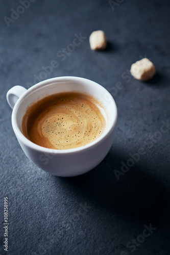 Cup of coffee and two brown sugar cubes on dark stone background. Close up.