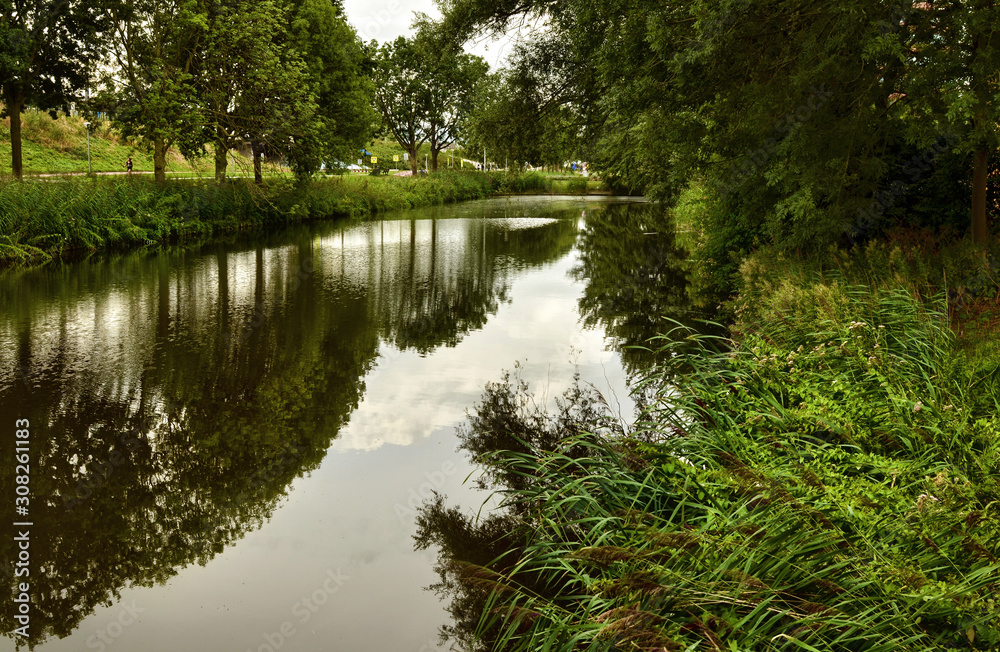 Amsterdam, Holland, August 2019. On the outskirts the canals are lined only with trees and greenery. The foliage is reflected in the water. Amsterdam, Holland, August 2019. On the outskirts the canals are lined only with trees and greenery. The foliage is reflected in the water.