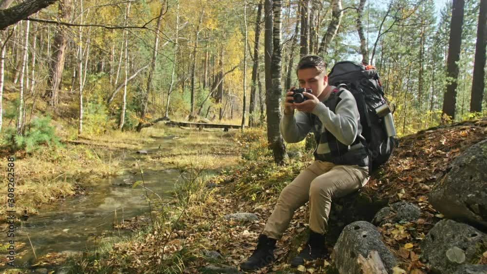 Traveler photographing scenic views in forest by mountain river. Man shooting picturesque views. The guy takes photo and video on dslr camera. Professional photographer traveler. Traveler photographing scenic views in forest by mountain river. Man shooting picturesque views. The guy takes photo and video on dslr camera. Professional photographer traveler.