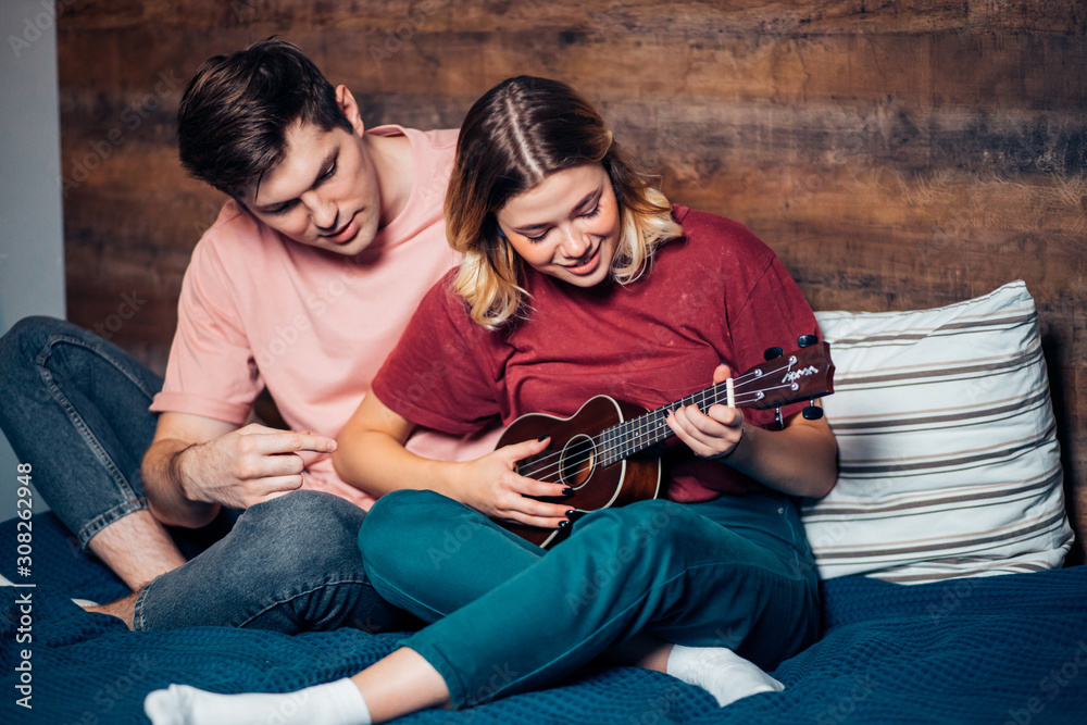 young beautiful caucasian woman playing ukulele at home, self-taught. wearing casual wear, t-shirt and jeans young beautiful caucasian woman playing ukulele at home, self-taught. wearing casual wear, t-shirt and jeans