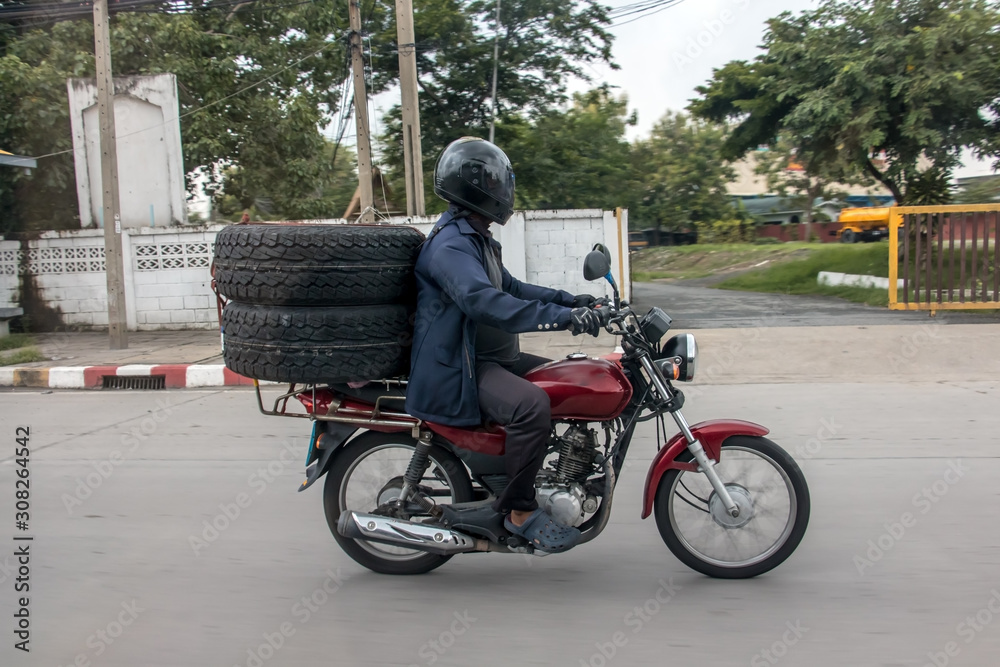 Transporting tires on a motorcycle. Man carries big tire on motorbike, Thailand.