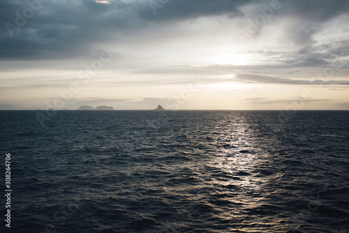 Nordic authentic view of sunset ocean and cloudy mountains. Severe landscape of rock in the distance among sea