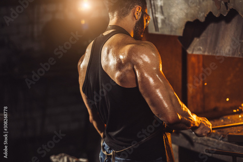 handsome blacksmith guy with muscular body, wearing gloves for safety, isolated in workshop