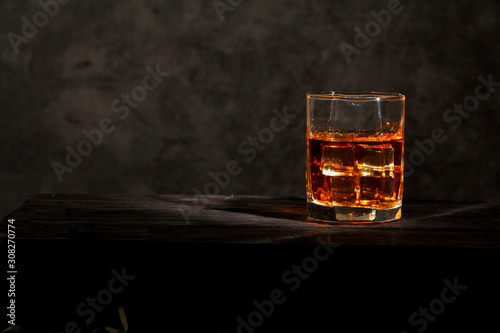 Whiskey with ice or brandy in a glass with lemon on a background of gray concrete on an old wooden table. Whiskey with ice in a glass. Whiskey or brandy. Selective focus.