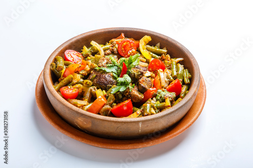 Chicken liver with vegetables on a clay plate. Pieces of liver, onion, string beans, tomato.  white background