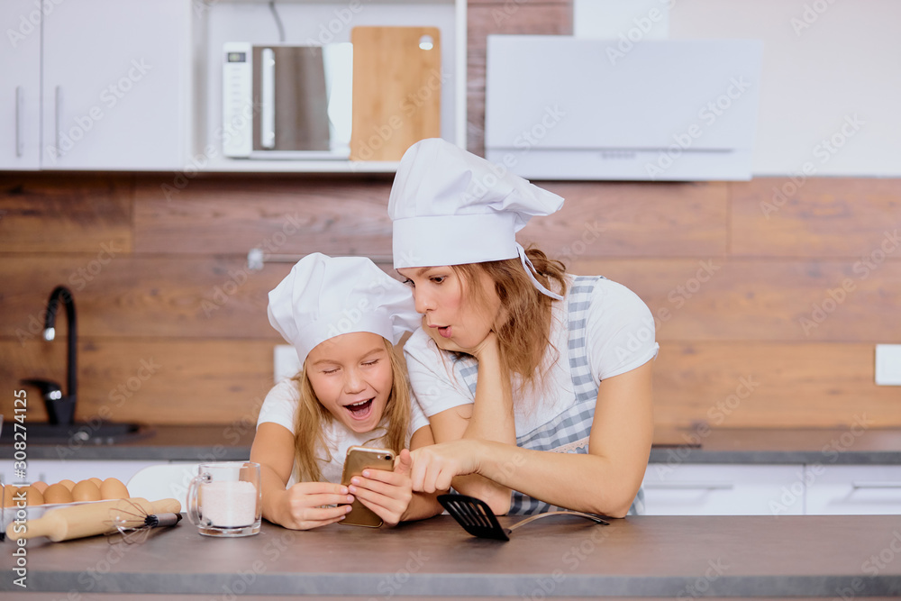 positive cheerful woman and child looking at smartphone before cooking positive cheerful woman and child looking at smartphone before cooking