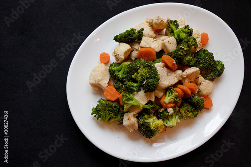Healthy fast dish. Easy home cooking. Broccoli, carrot, chicken breast and spices. On the white dish and black background. Smell.