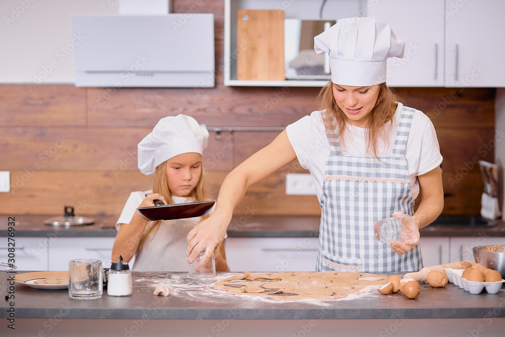 mother and child together in kitchen, happy baking at home. little girl help to bake, to form dough, to make dough with use of chicken eggs and flour, wearing white caps and aprons. enjoy making food mother and child together in kitchen, happy baking at home. little girl help to bake, to form dough, to make dough with use of chicken eggs and flour, wearing white caps and aprons. enjoy making food