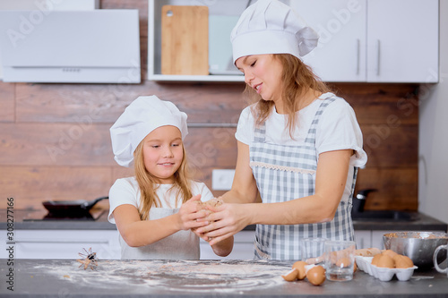 caucasian mother with child in kitchen. little girl help mother to make dough for baking cakes