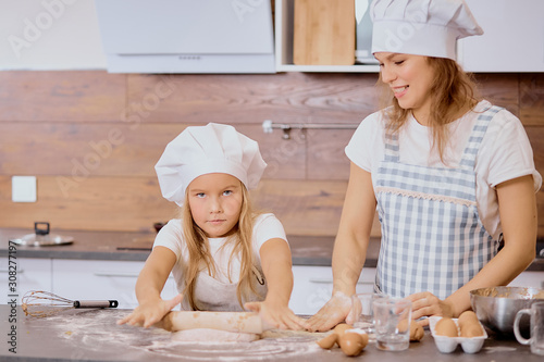 cute kid girl preparing dough for future baking cake with mother, mother look at her and smile. wearing aprons
