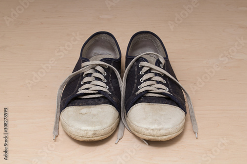 Old dirty shabby sneakers over light wooden background