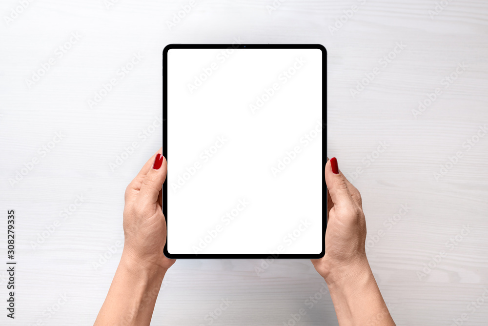 Tablet mockup. Girl holding tablet in vertical position abowe white desk. Flat lay, top view - obrazy, fototapety, plakaty 