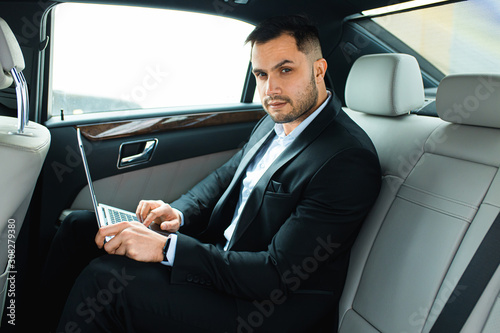 handsome young businessman sit with laptop while working in car, man looking at camera © alfa27