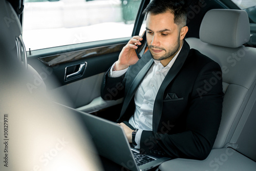 elegant young man with beard talking on phone, process of working in car, talk with his business colleague © alfa27